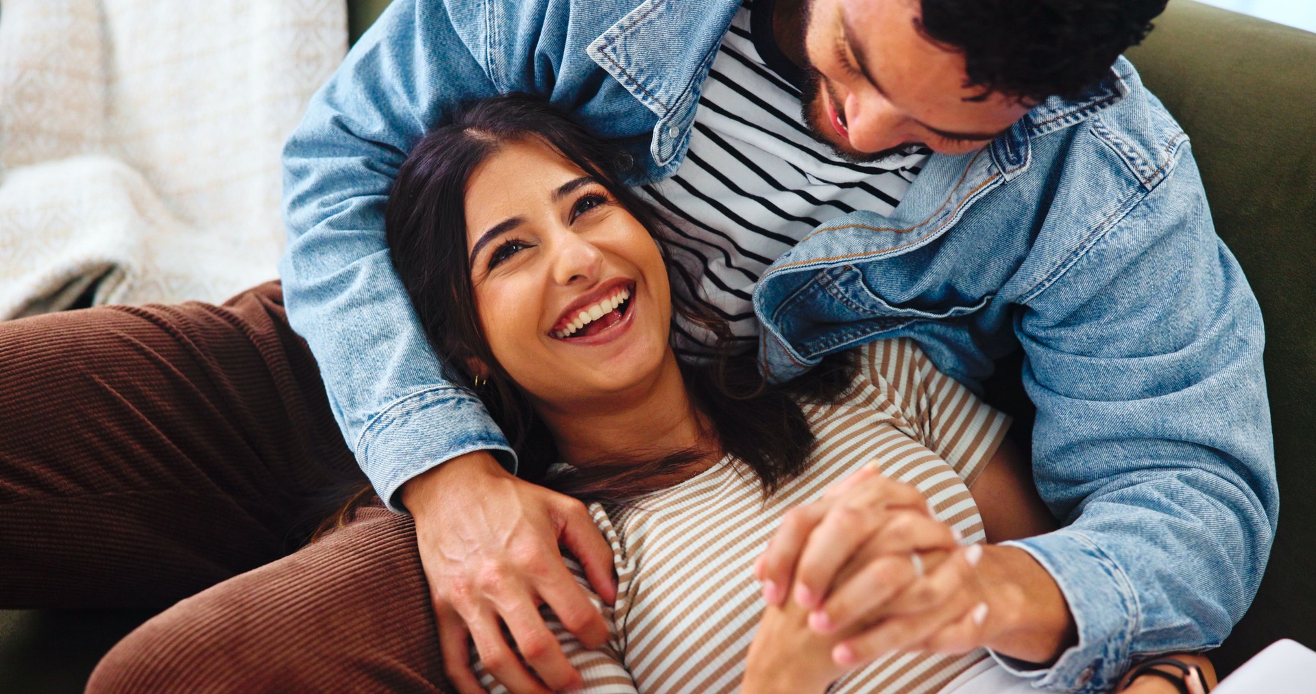 Happy couple, relax and laughing with sofa for funny joke, bonding or humor together at home. Woman, man and young lovers with smile, comedy or weekend for holiday romance, love and comfort at house
